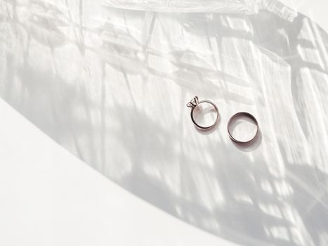 Top view on wedding and engagement rings with diamond. Symbol of love and marriage on white background with laced shadow. Sunlight on white background.