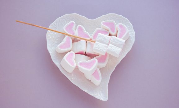 Heart-shaped marshmallow on a white plate on a pink background. The concept of mother's Day, Valentine's Day.