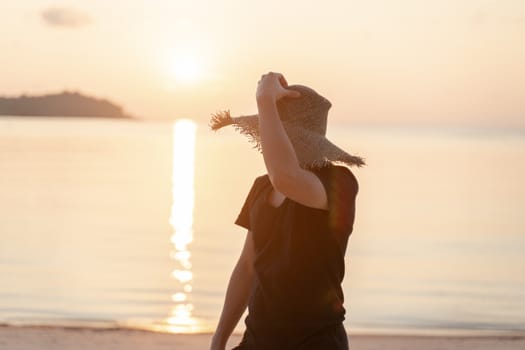 Man in black T-shirt and straw hat enjoying beautiful sunrise or sunset on the beach.