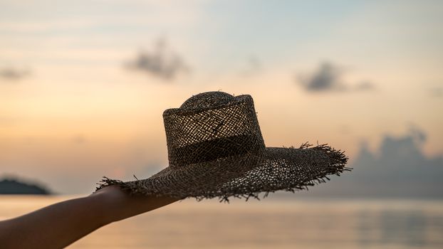 Female hands hold summer straw hat with sunset view. Vacation concept