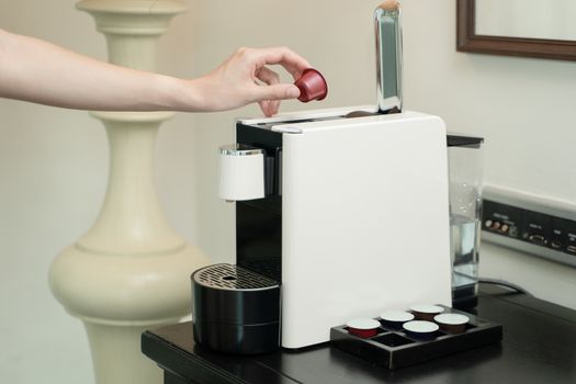 Close up of woman hand pressing button on a capsule into a coffee machine.