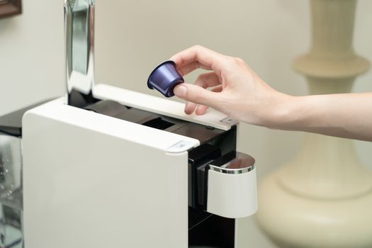 Close up of woman hand pressing button on a capsule into a coffee machine.