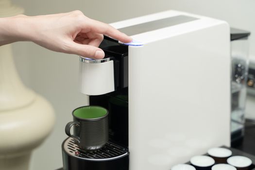Close up of woman hand pressing button on a capsule into a coffee machine.