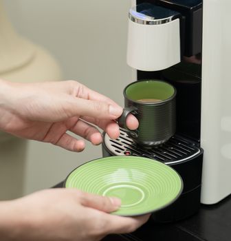 Machine serving coffee in a cup. Coffee capsule machine maker. Hand holding a ceramic cup of coffee on the coffee machine.