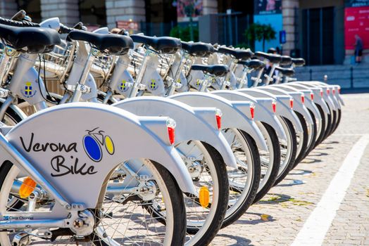 Verona, Veneto/Italy - 18.08.2020: A row of electric bicycles photographed from behind in the sun in the city of Verona for rent to tourists. On the bikes is written Verona Bike