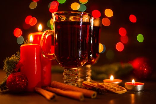 Mulled wine with cinnamon sticks orange candles fir tree branch and baubles over holiday christmas lights background