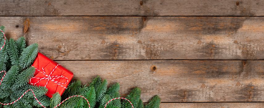 Christmas noble fir tree twigs and gift with red striped ribbon on wooden background with copy space for text