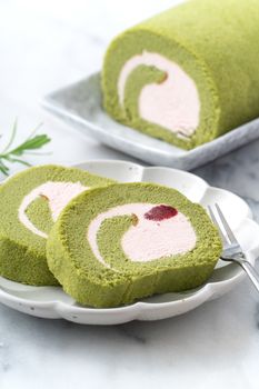 Delicious Matcha Swiss Roll Cake slices with strawberry icing cream on white background, close up.