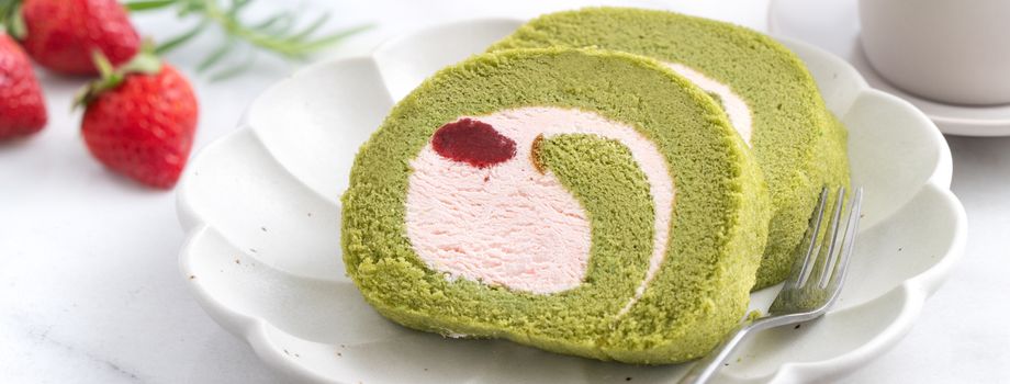 Delicious Matcha Swiss Roll Cake slices with strawberry icing cream on white background, close up.