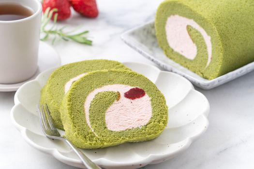 Delicious Matcha Swiss Roll Cake slices with strawberry icing cream on white background, close up.