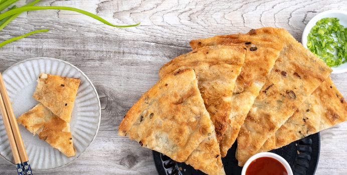 Taiwanese food - delicious flaky scallion pie pancakes on bright wooden table background, traditional snack in Taiwan, top view.