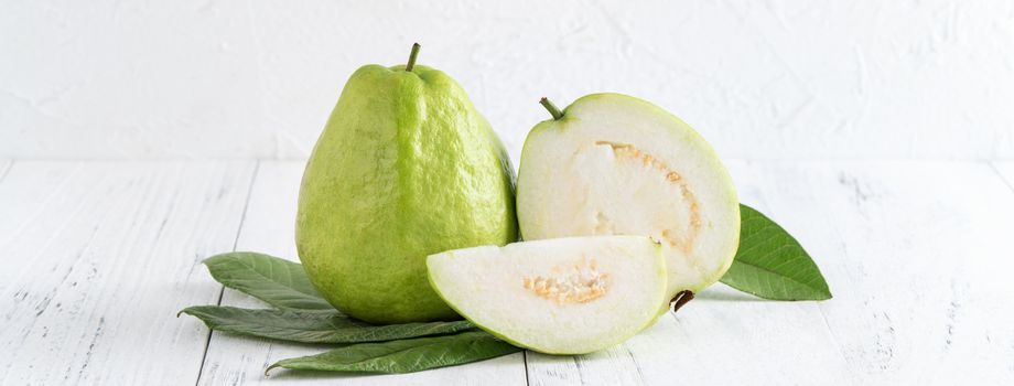 Delicious beautiful guava set with fresh leaves isolated on bright white wooden table background, close up.