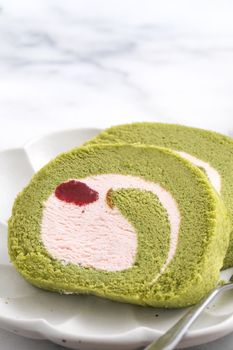 Delicious Matcha Swiss Roll Cake slices with strawberry icing cream on white background, close up.