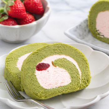 Delicious Matcha Swiss Roll Cake slices with strawberry icing cream on white background, close up.