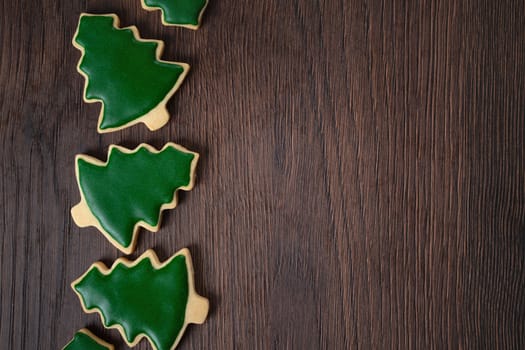 Top view of decorated green plain flavor gingerbread Christmas tree cookie on wooden table background with copy space, concept of holiday celebration.