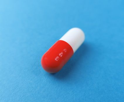 Red and white macro single pill capsule on a blue background.
