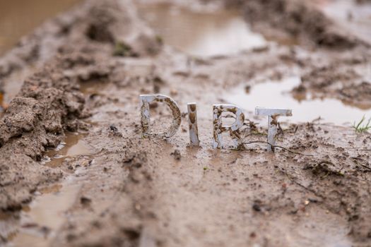 the word dirt composed of silver metal letters on wet clay surface with selective focus, background blur and linear perspective in cloudy autumn day light