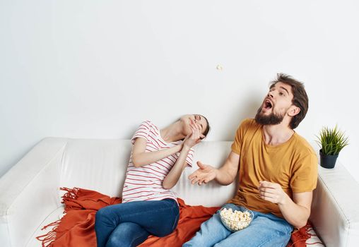 Fun man and energetic woman watching TV on the couch popcorn in a plate family communication. High quality photo