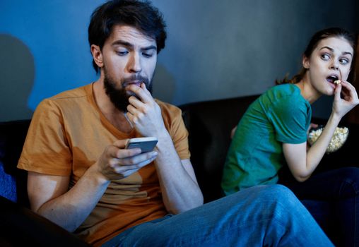 Emotional woman and man on the couch with popcorn watching TV. High quality photo