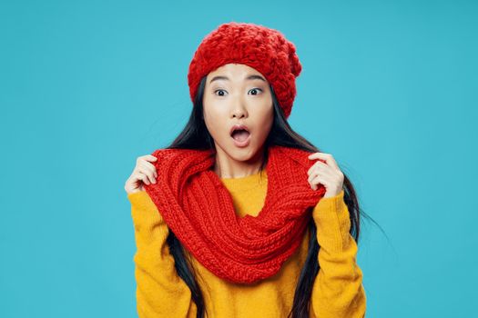 Surprised Asian woman in a scarf and hat on a blue background opened her mouth wide