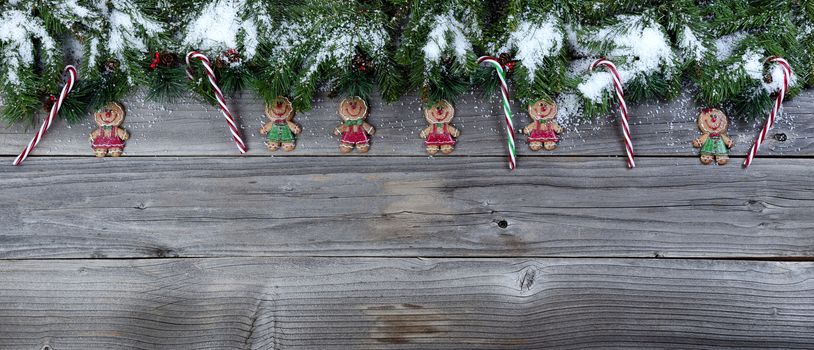 Christmas rustic natural wooden background with snow covered evergreen branches and Gingerbread cookie figures plus candy canes  
