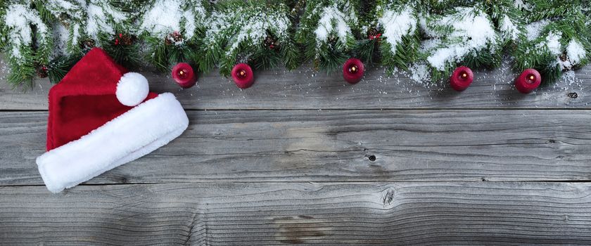 Merry Christmas concept on rustic natural wooden background with traditional holiday decorations of candles and Santa cap   