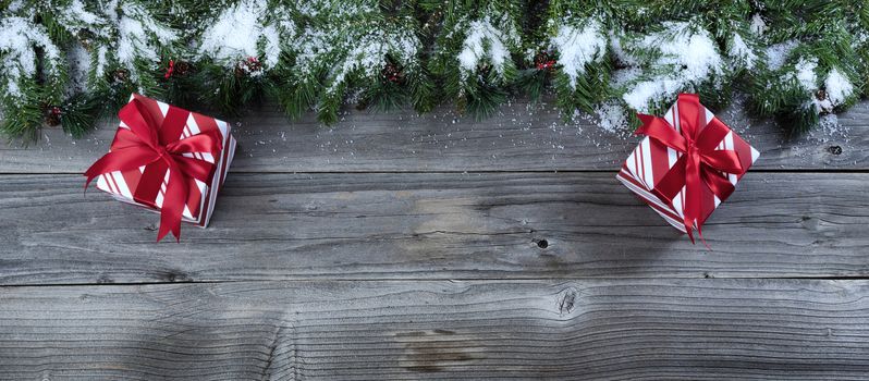 Merry Christmas concept on rustic natural wooden background with snow covered Fir branches plus wrapped giftboxes   