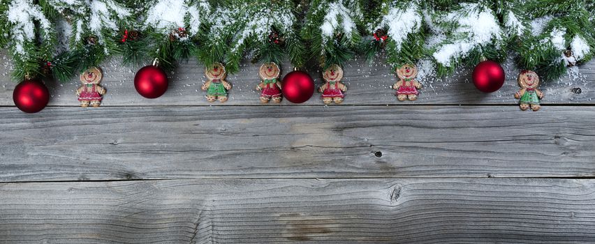 Christmas rustic natural wooden background with snow covered evergreen branches and Gingerbread cookie figures plus red ball ornaments   