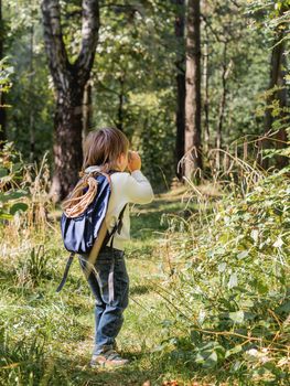 Curious boy is hiking in forest. Outdoor leisure activity for kids. Child looks through binoculars on tree foliage. Sunny day at autumn or summer day.