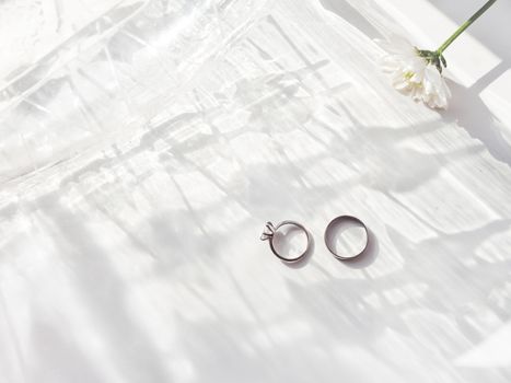 Top view on wedding and engagement rings with diamond. Symbol of love and marriage on white background with laced shadow. Sunlight on white background.