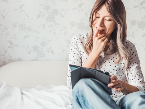 Woman sits on bed with tablet PC. She watches online TV series. Online video call or conference, distance learning, remote education. Self isolation during quarantine.