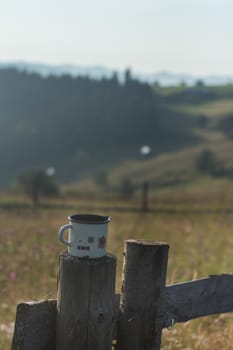 Metal mug in nature with mountains - metal mug on the fence in the morning