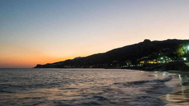 Sea shore at the sunset with mountains behind and little waves