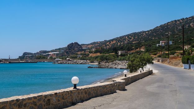 Road and sea in Keratokampos, Crete with a small port and olive trees on the mountain