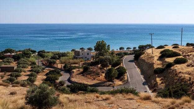 Bending road through the lands with olive trees and Libyan sea further away - Crete