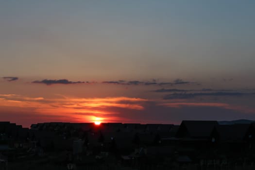 Sunset behind the houses with orange sky and clouds