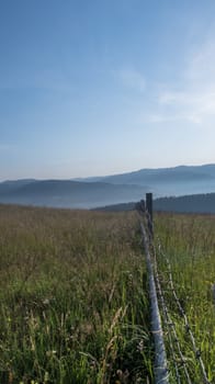 Fence with grass field directing to mountains - morning landscape of mountains in Romania