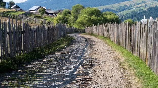 Road with ballast in the mountains with houses - fence in the mountains