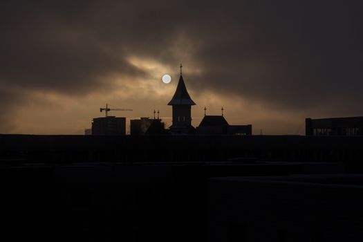 Fade sunrise with fog and dark sky with silhouette church and buildings - hazy sky and sun