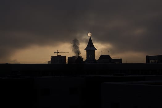 Fade sunrise with fog and dark sky with silhouette church and buildings and sun behind the buildings