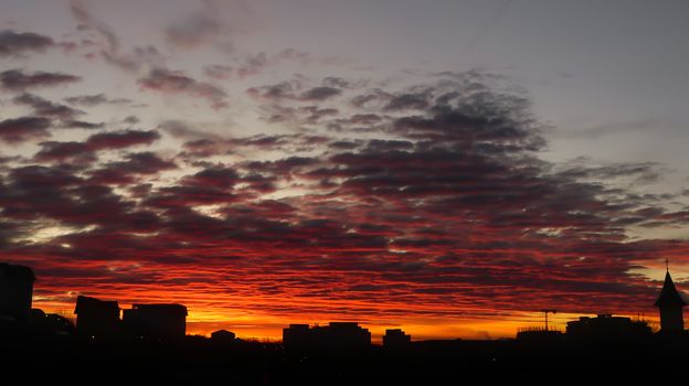 Cloudy fire sunrise with backlit buildings and cloudy sky. Landscape of fire sunrise