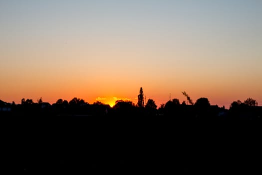 Sunset over city. Silhouette and backlit houses and trees