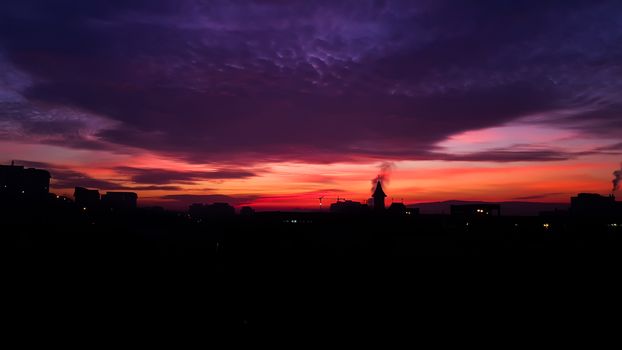 Purple and orange dramatic sunrise with clouds and backlit city and buildings in the morning