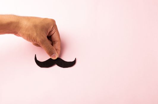 The man uses hand holding black mustache, studio shot isolated on white background, Prostate cancer awareness month, Fathers day, minimal November moustache concept