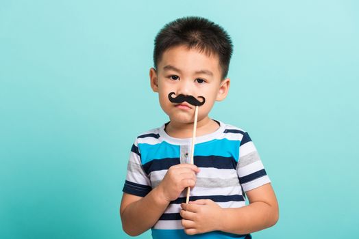 Funny happy hipster kid holding black mustache props for the photo booth close face, studio shot isolated on a blue background, Men health awareness, Prostate Cancer Awareness