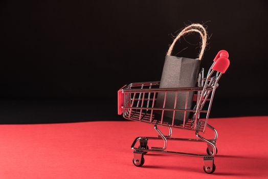 Black Friday sale shopping concept, Black shopping bags in a shopping cart, studio shot isolated on red and black background