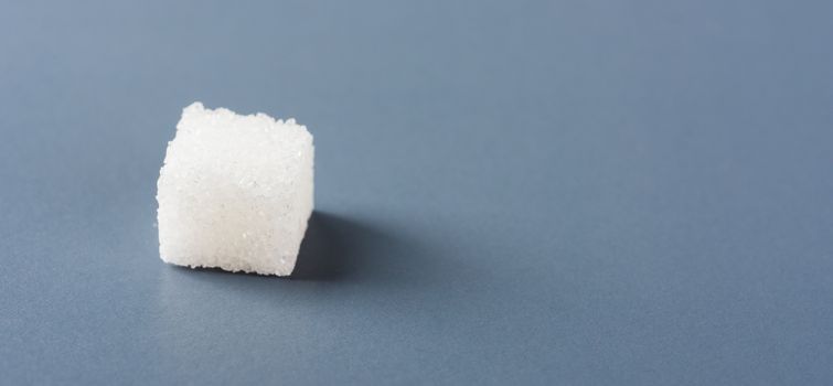 One white sugar cube sweet food ingredient, isolated on a gray background, health high blood risk of diabetes and calorie intake concept