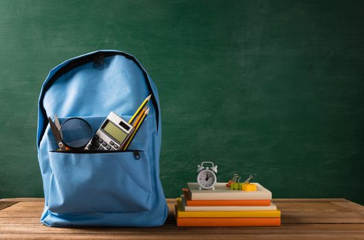 Front of stylish school bag backpack and stationery accessory on a table desk at the green chalkboard, Back to school education concept