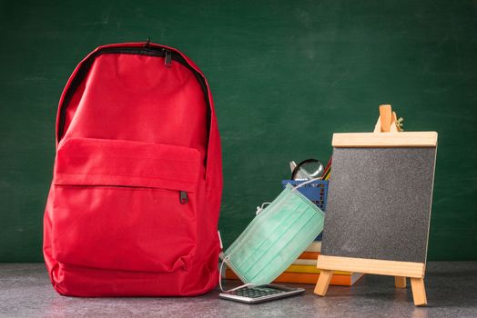 Front school backpack and accessories with face mask protect on table at chalkboard, student bag supplies at classroom backboard, Back to school education new normal outbreak COVID-19 or coronavirus