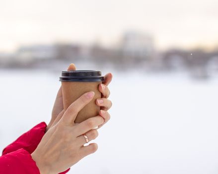 A young woman in a red jacket in winter holds a glass of hot coffee or tea. A snowy winter and a hot drink to keep you warm. A glass of coffee in winter.